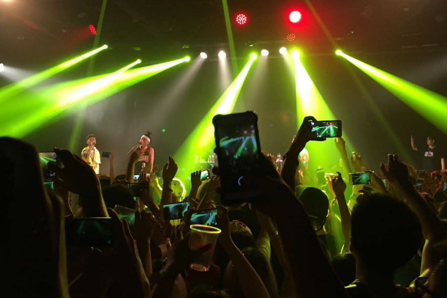 Photo of Higher Brothers performing onstage infront of a large crowd with lights beaming everywhere.