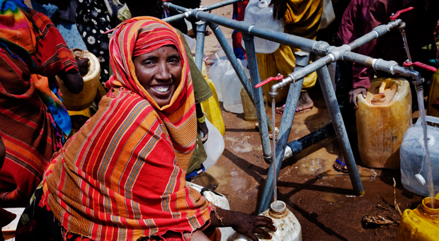 Several Kenyan women are filling large plastic bottles with water from a multiple-outlet tap.