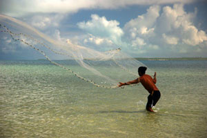 Man in knee-high water throwing a fishing net