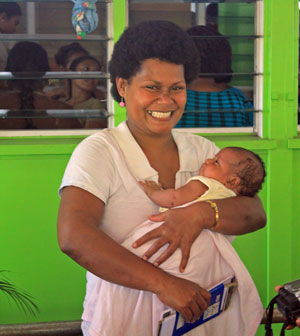 A smiling Fijian woman holding a baby