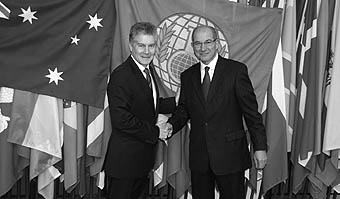 Photo of Mr Smith shaking hands with Ambassador Üzümcü in front of international flags.