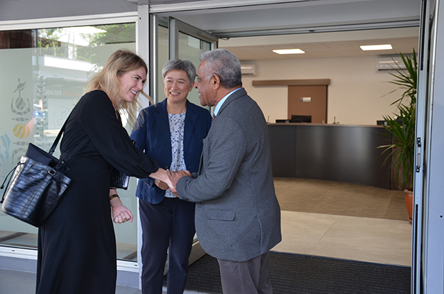 Two women greet a man in the entrance to an office space.