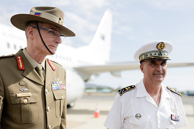 Two men in military uniform smiling in front of a military aircraft.