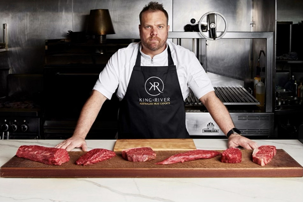 A butcher standing behind a counter, displaying butchered meat.