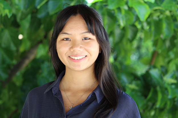 Young woman smiling, standing outside under lush green leaves