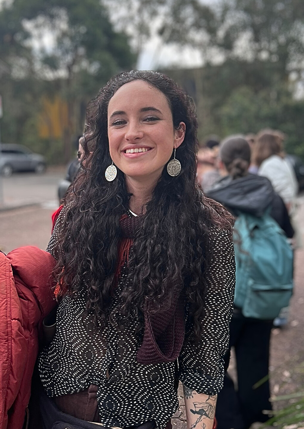 Alinta smiling who has long curly hair and is holding a red jacket