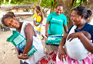 Four women holding babies or bed nets, and laughing