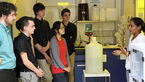 Group of students listening to a scientist in a lab coat.