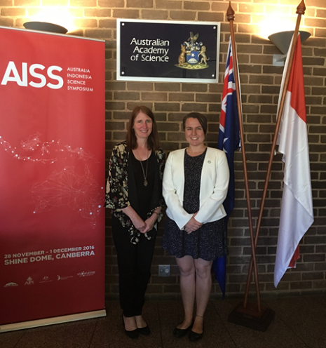 Cherie standing with another woman under an Australian Academy of Science sign, between an Australia Indonesia Science Symposium banner and the Australian and Indonesian flags.