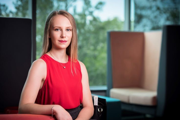 A woman with blond hair, wearing a red sleeveless shirt, seated in a corporate office setting.