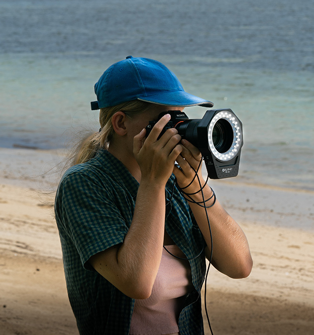 Women on a beach with a camera held up to her face