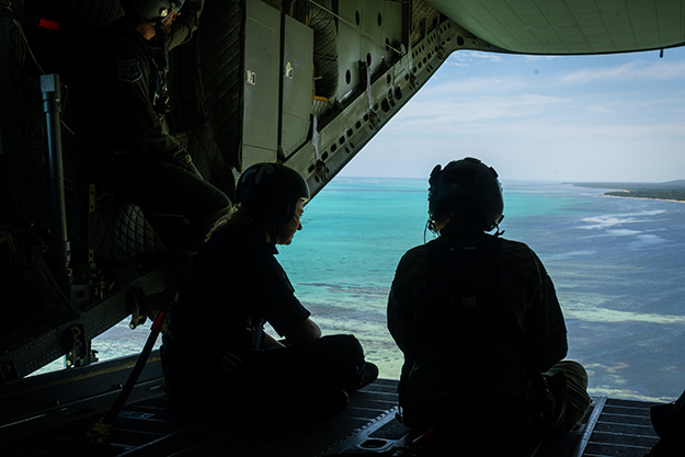 Two people sitting on the ramp of an aircraft while it fly's over a reef