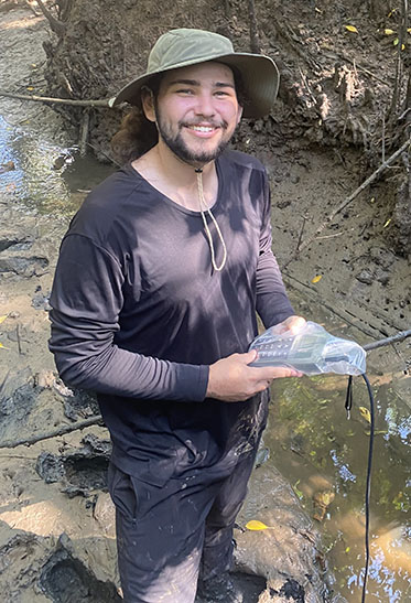 Man in a hat standing in a river with a plastic bottle in his hands.