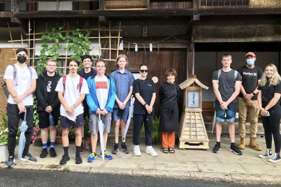 Eleven people posing for a photo in front of an old wood building