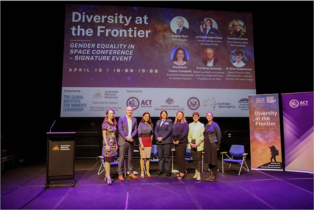 7 people standing on a stage with large screen behind them