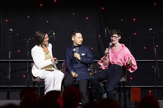 Three people sitting on a stage with microphones 