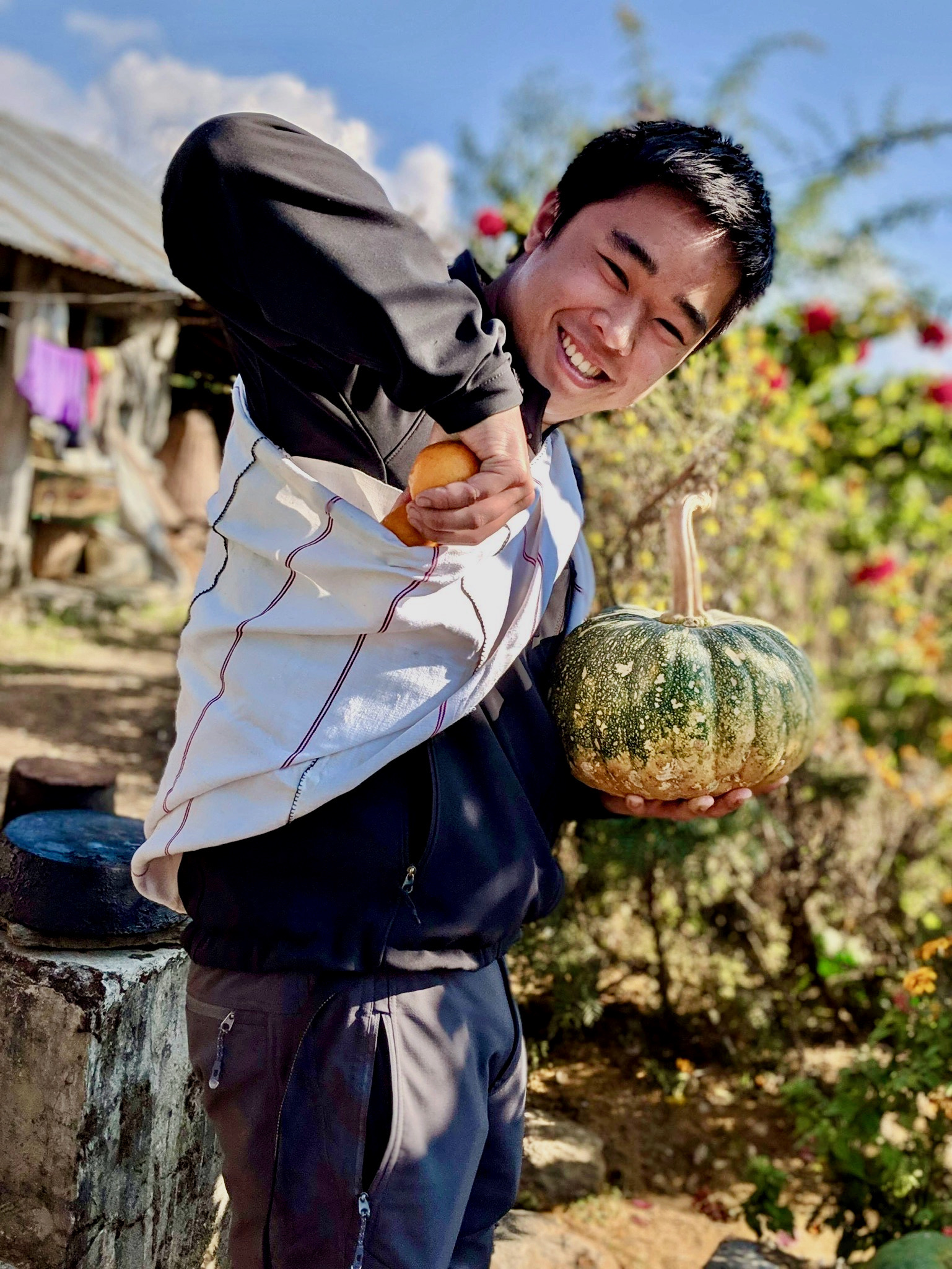 Photo of Andy Tran in a garden holding a fruit and vegetable. 