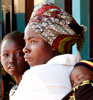 Photo of a mother and father, with their child sleeping on the father's back.