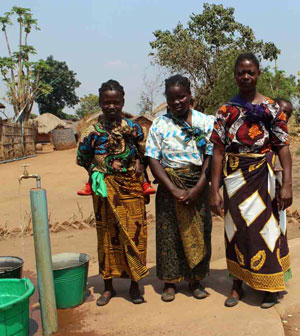 Photo of three women standing next to a safe water pump.