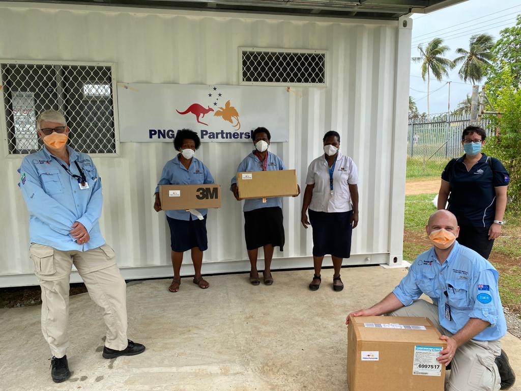 Three PNG frontline workers and three AUSMAT team members – wearing masks -pose for a photo with boxes of PPE in Vanimo, PNG