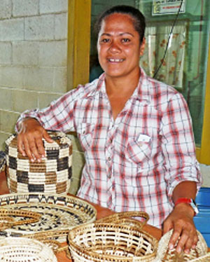 Young woman from Tonga standing in front of a display of three woven baskets.