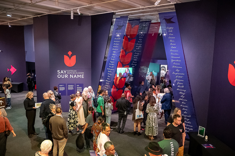 A crowd of people gathered at a Say Our Name exhibition.