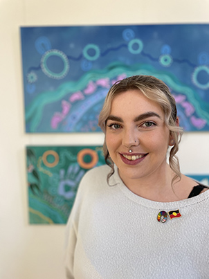 Indigenous woman standing in front of her artwork.