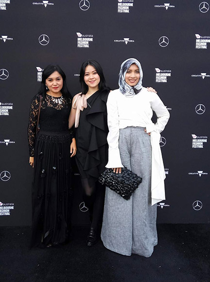 Three women standing together in front of a Melbourne Fashion Festival media wall