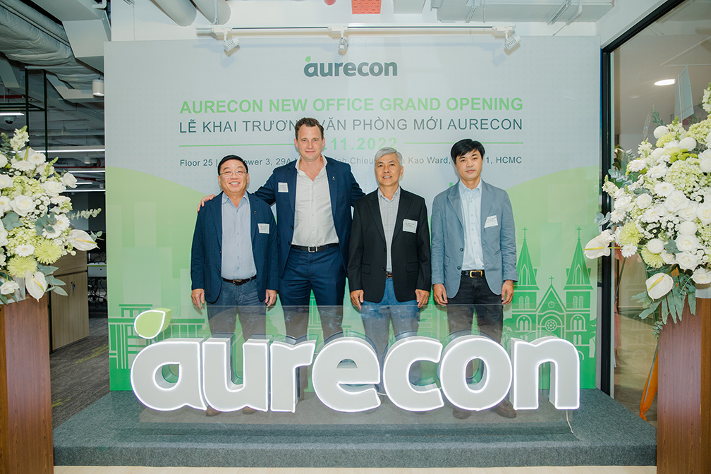 Four men standing behind a neon ‘Aurecon’ sign.	