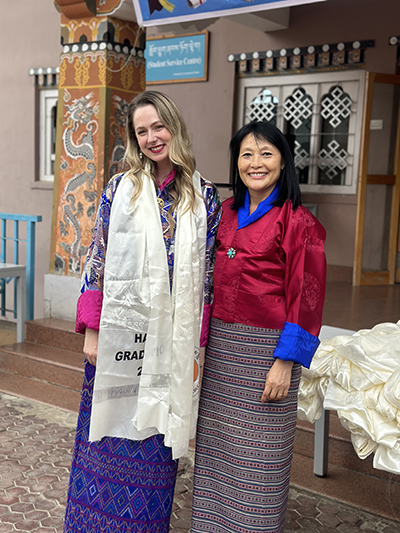 Samantha wearing a graduation scarf, standing with another woman wearing traditional Bhutanese clothing.