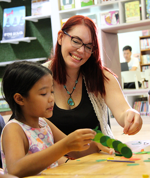 Sara at a table with a young girl working on crafts