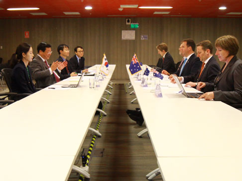 Korean delegates on one side of a meeting table and Australian delegates on the other side.