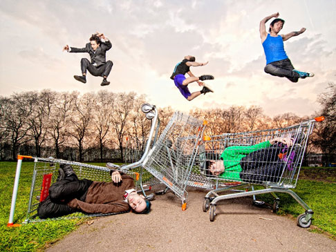 Shopping trolleys with people inside them and more epople jumping in the air above them.