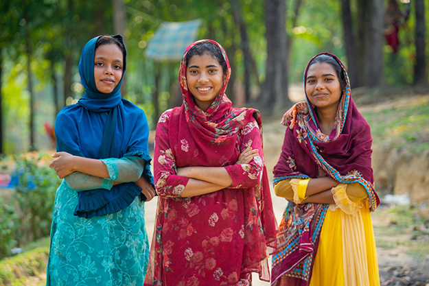 Three Bangladesh girls standing side by side dressed in colorful sarees