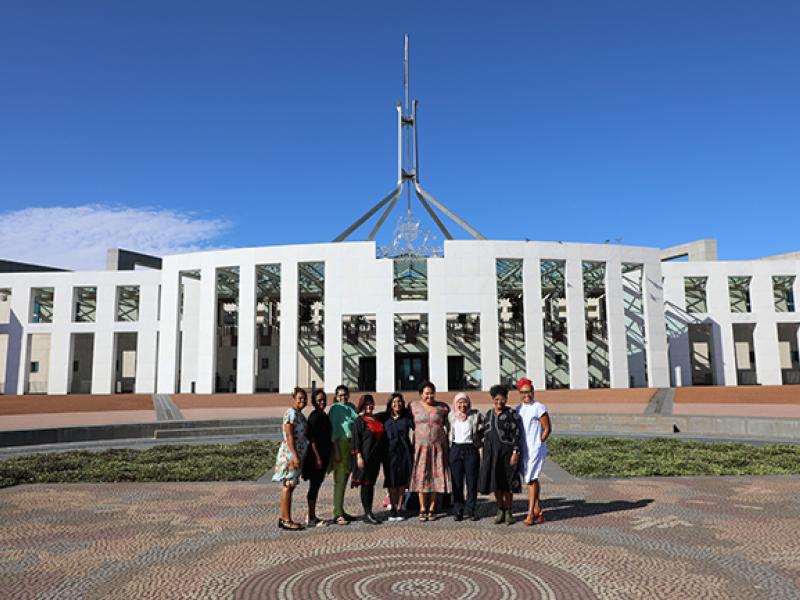 Nine women standing together in front of Parliament House in Canberra, Australia. 