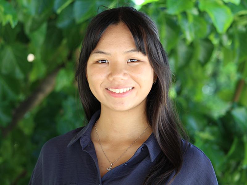 Young woman smiling, standing outside under lush green leaves