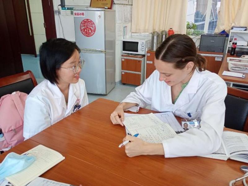 Two women seated at a desk, one woman taking notes while another speaks.