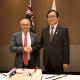 The Hon Don Farrell, Minister for Trade and Tourism, Australia and Dr Cheong Inkyo, Minister for Trade, the Republic of Korea, are smiling and shaking hands while standing behind a cake that is celebrating the 10-year anniversary of the Korea-Australia Free Trade Agreement. An Australian and a Korean flag are behind the ministers.