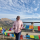 Harine leaning back on a railing, draped with flags up on top of a mountain