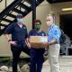 Two Australian medical specialists stand next to a Papua New Guinea frontline worker, presenting a box that contains an inline suction device for the Port Moresby General Hospital.