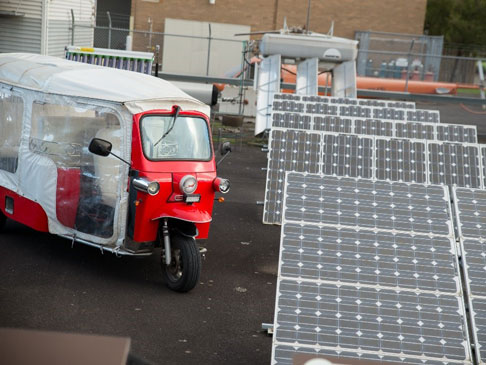 Photo of Tuk Tuk next to solar panels.