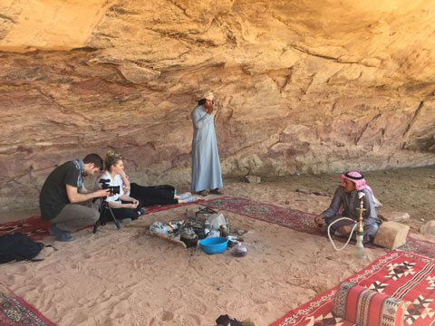 Two people taking a photo of a man sitting in a sandy cave.