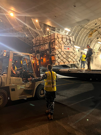 A forklift offloads a pallet of Australian aid supplies from the back of a military aircraft.